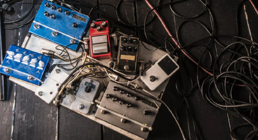 Messy and noisy guitar pedalboard with tangled cables on a dark floor.