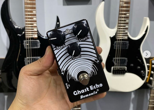 Demonfx Ghast Echo pedal held in hand, with electric guitars in the background.