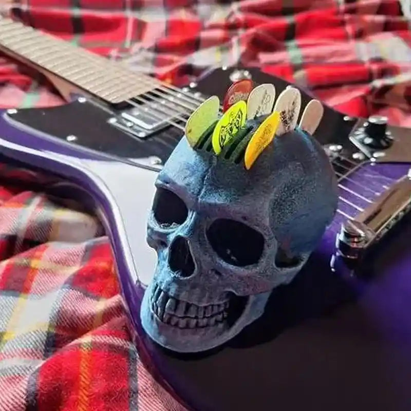 Skull guitar pick holder with a realistic skull design and Mohawk-style pick arrangement, holding 21 picks, displayed on a purple electric guitar over a plaid fabric.
